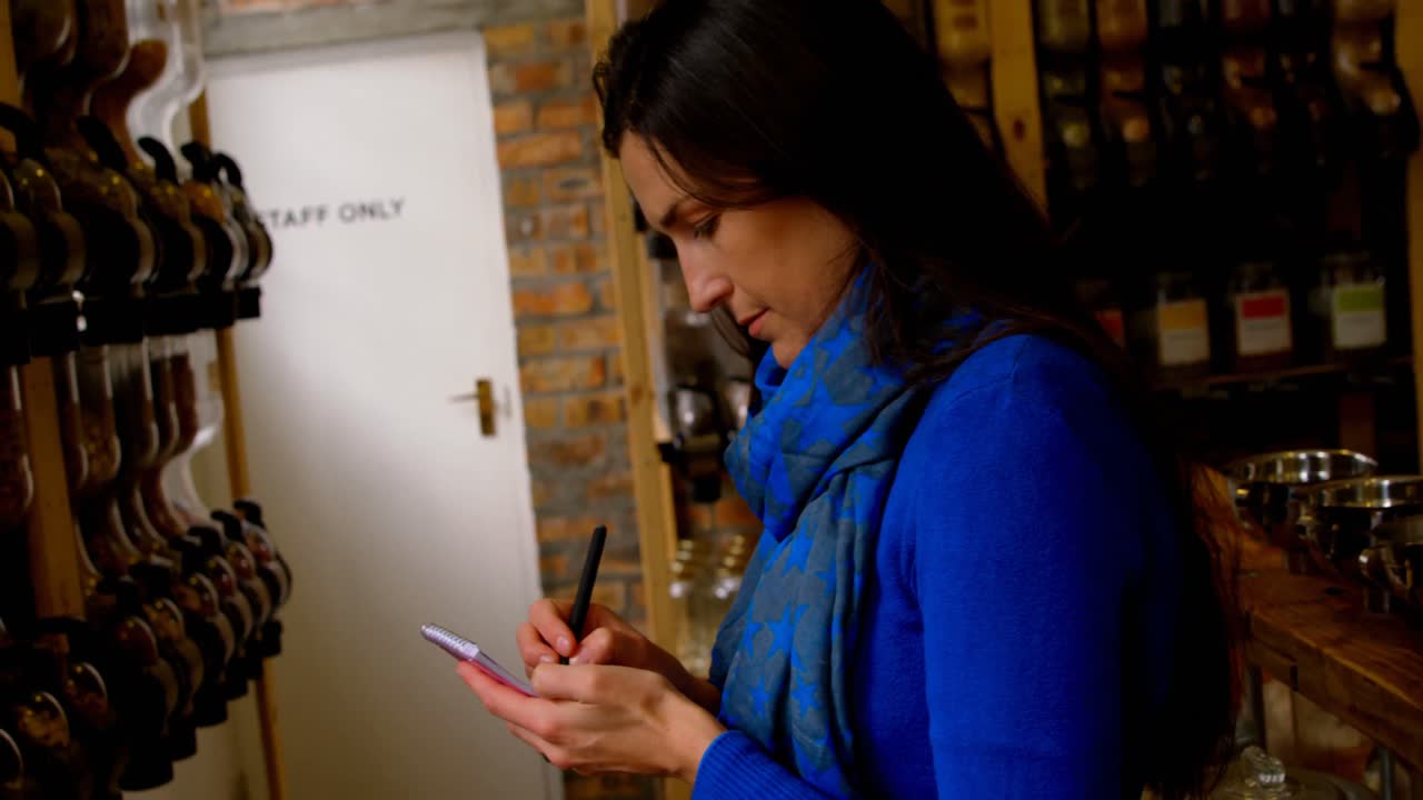 Side view of woman writing on notepad in supermarket 4k
