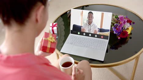 Mujer-Birracial-Sosteniendo-Un-Regalo-Y-Hablando-Con-Un-Hombre-Birracial-Hablando-En-La-Pantalla-Del-Portátil