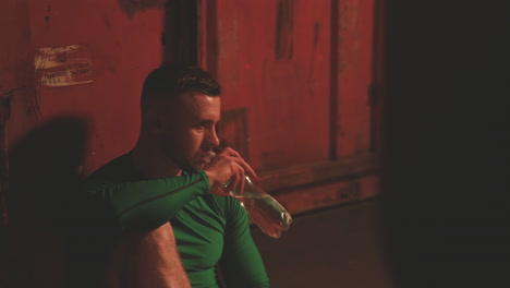 male boxer rests and drinks water sitting next to the punching bag