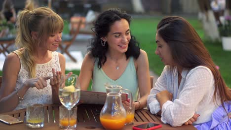 Three-beautiful-women-having-fun-choosing-meal,-looking-at-the-menu,-laughing-and-gesturing