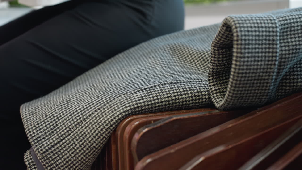 Close up of modern wooden bench in public space as person partially visible drops cloth on surface and begins to sit, showcasing detailed bench slats and clean interior with soft natural lighting
