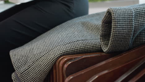 close up of modern wooden bench in public space as person partially visible drops cloth on surface and begins to sit, showcasing detailed bench slats and clean interior with soft natural lighting