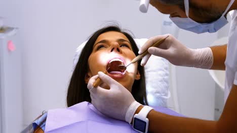 Dentist-examining-a-female-patient-with-tools