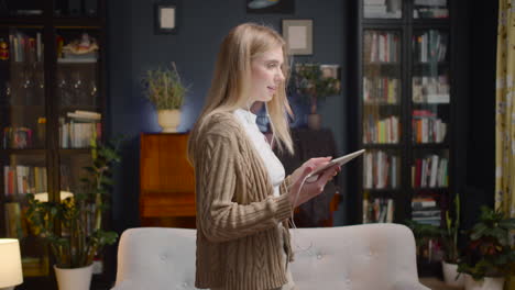 happy young woman with earphones listening music on tablet and dancing while walking in living room