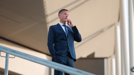 Low-angle-shot-of-a-mature-businessman-standing-on-top-of-the-stairs-making-a-call