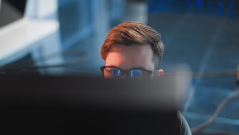 person focused on video control panel in tv studio, observing live footage on screen, with reflection visible in glasses, background featuring high-tech broadcast setup