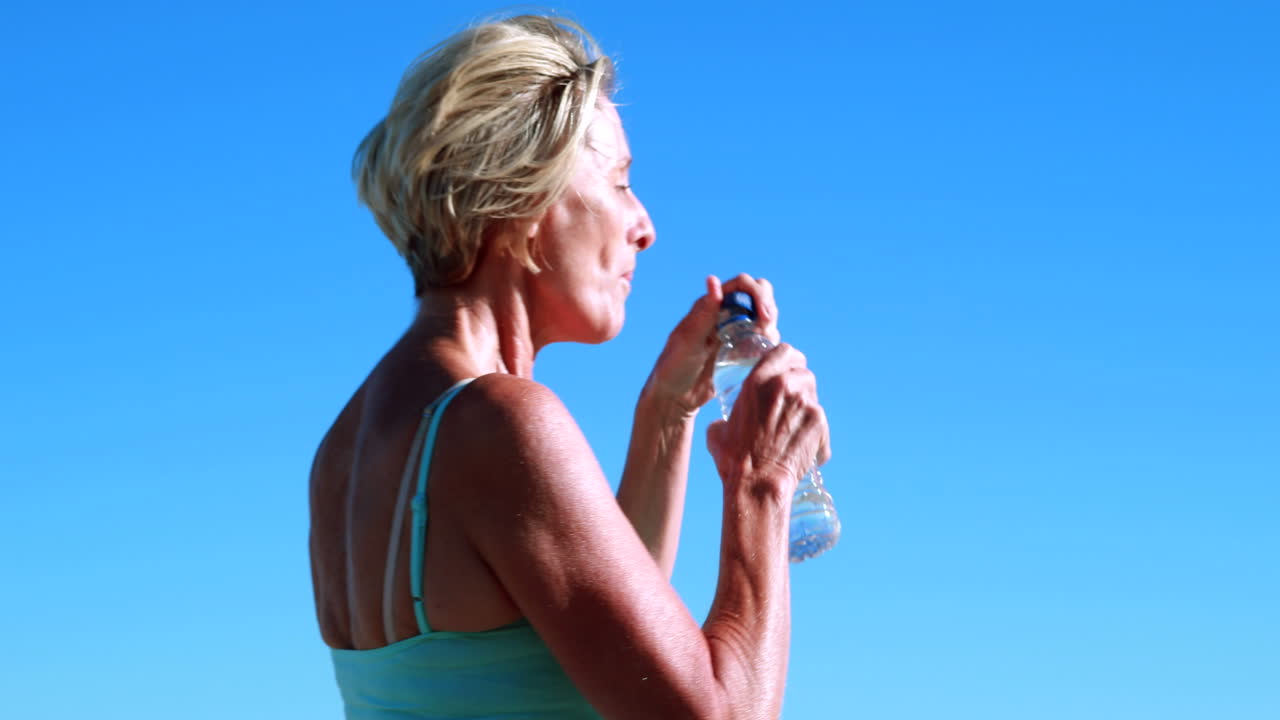 Donna anziana in forma che si ferma durante la corsa per bere.