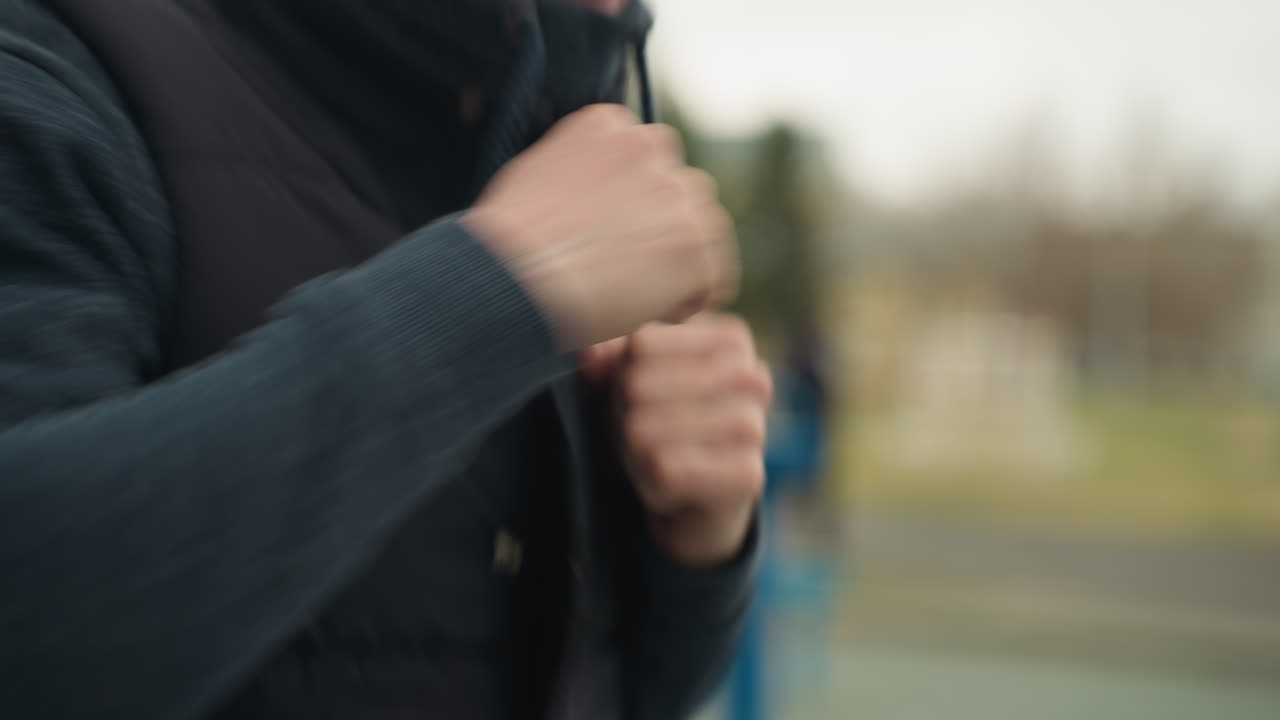 Close-up of a person jogging while wearing a black jacket, with clenched fists, with a blur view of someone passing with the background blur