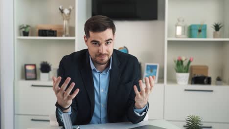 El-Retrato-Muestra-A-Un-Hombre-Confiado-Y-Sonriente-Vestido-De-Negocios-Sentado-En-Una-Oficina-Prestigiosa,-Gesticulando-Mientras-Comparte-Algo-Positivo