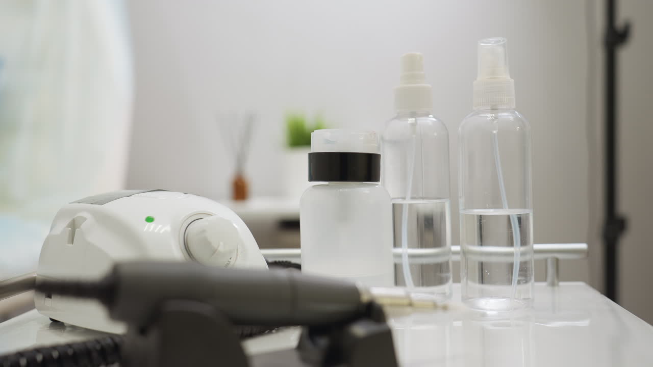 Close up view of transparent spray bottles and lotion dispenser placed beside electric control device on clean white table in modern salon setup with blurred background featuring decorative items