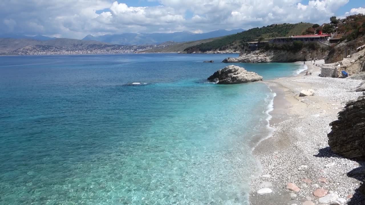 paradisiacal Pulebardha Beach in Ksamil, Albanian riviera. Saranda city on background
