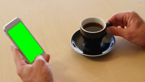 Businessman-using-mobile-phone-while-holding-a-cup-of-coffee