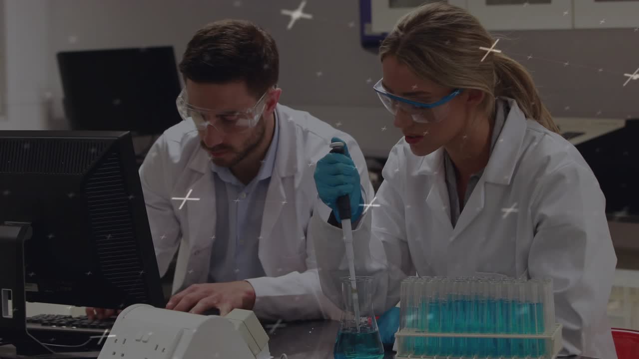Man at lab computer typing while woman lifting pipette and transferring blue liquid for sample prep