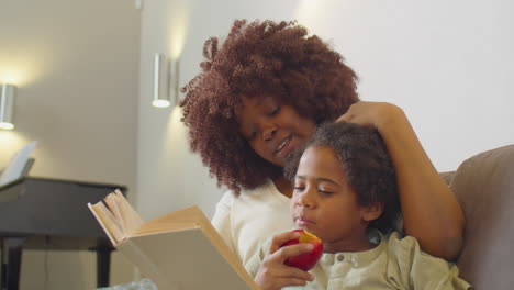 boy eating apple and reading book with mom at home