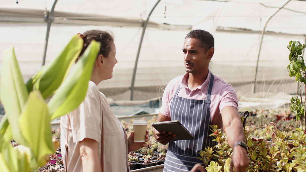 In greenhouse, gardening diverse enthusiasts discussing plant care surrounded by vibrant foliage