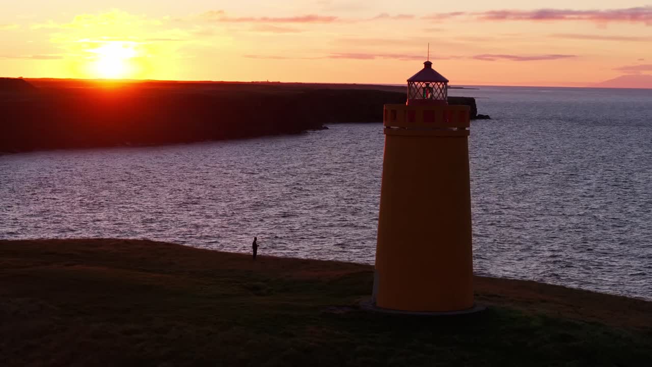 Una vista panoramica di un faro arancione in cima a una scogliera frastagliata durante un tramonto suggestivo all'ora d'oro in Islanda. Perfetto per documentari di viaggio e progetti paesaggistici cinematografici