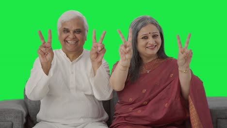 una vieja pareja india feliz mostrando el signo de la victoria en la pantalla verde.