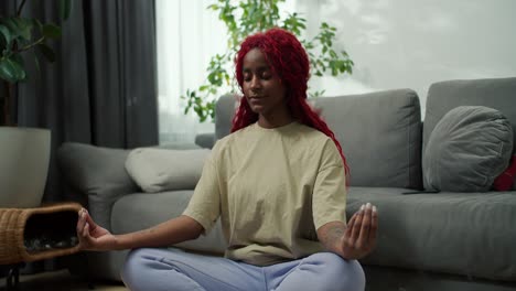 Young-stylish-african-american-woman-sitting-in-lotus-position-with-closed-eyes-healthy-calm-girl-relaxing-in-meditation