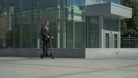 businessman riding an electric scooter in front of modern building