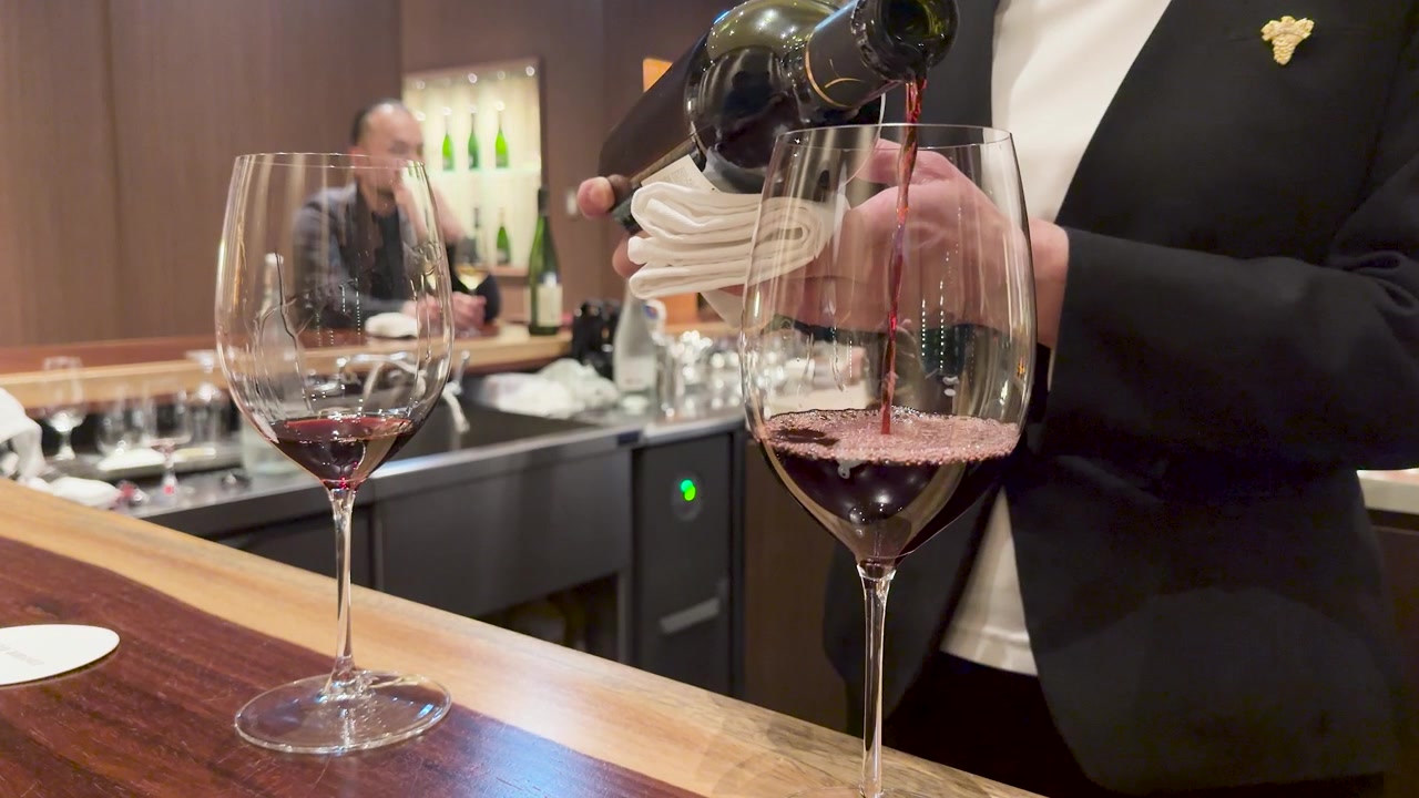 Een sommelier in pak schenkt rode wijn in een glas in een luxe bar.
