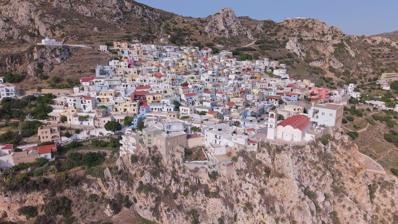 Pull-back drone footage revealing Menetes, a traditional colorful village on Karpathos Island, Greece, surrounded by scenic mountains and Mediterranean beauty