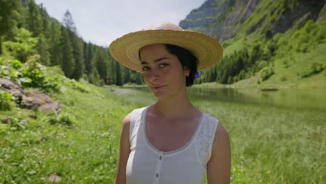 portrait shot of beautiful woman with straw hat in nature of switzerland. sunny day in summer season. green meadow and lake in background. close up. brunette short hairs and white skirt.