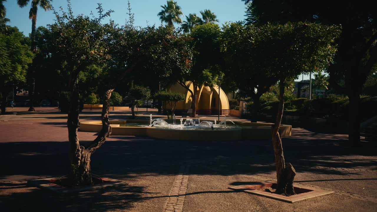 Piazza ombreggiata con piccola fontana e alberi circostanti.