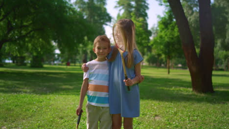 dos hermanos sonrientes posando con raquetas. niños juguetones abrazándose en el parque.