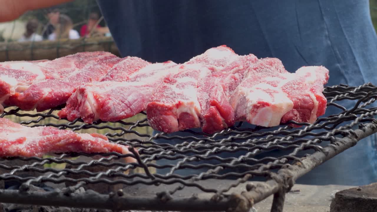 가족 과 친구 들 과 함께 바베큐 를 하기 위해 그릴 에 생고기 조각 을 놓고 있는 근접적 인 모습