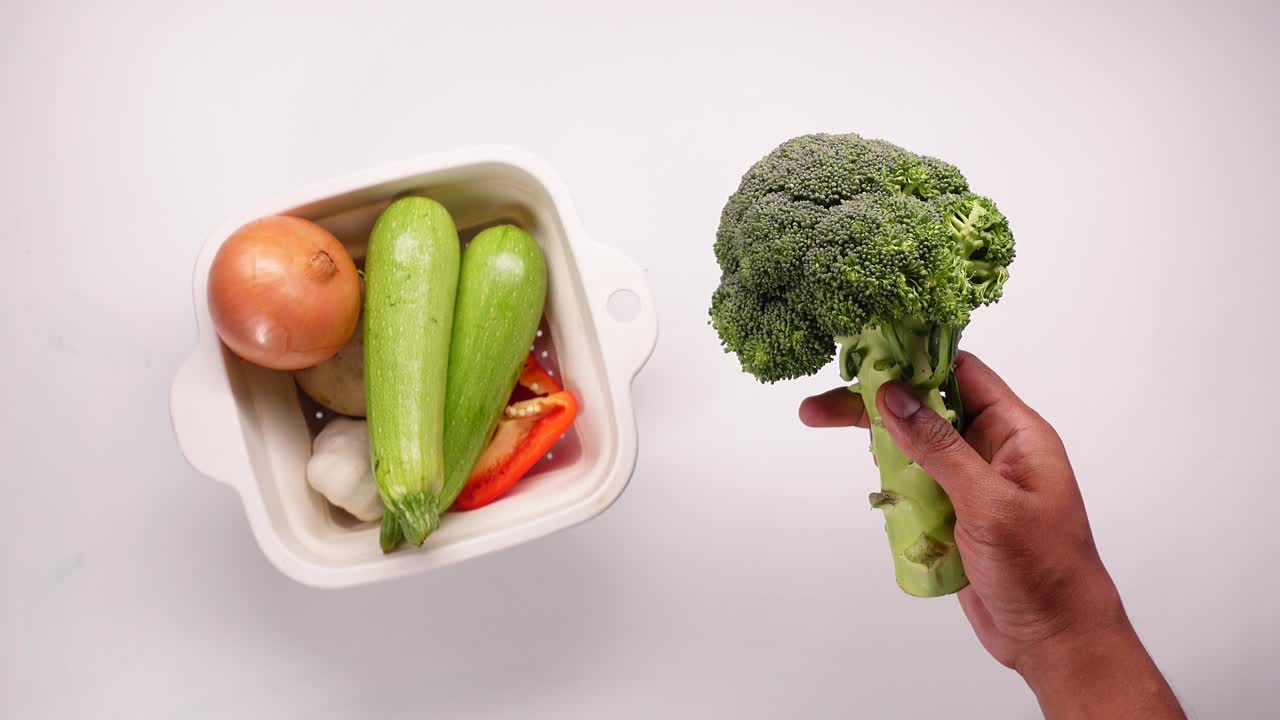 Mano che tiene broccoli freschi con verdure assortite in uno scolapasta