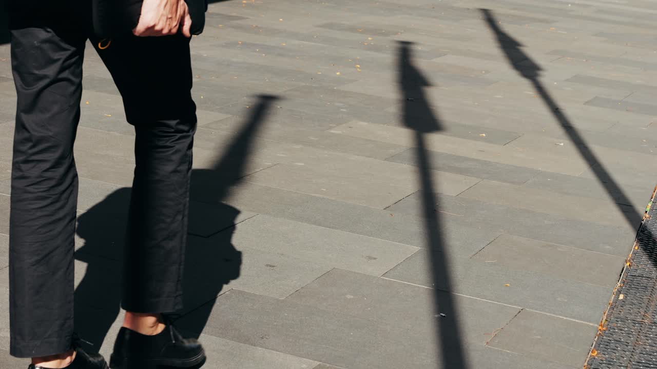 Una persona che cammina su un marciapiede proiettando ombre.
