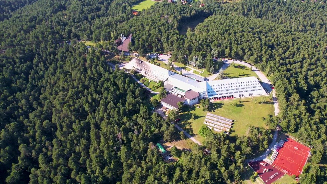 Dron krąży nad Hotelem Omorika na Górze Tara, ukazując kanciasty biały kompleks, rozległe trawniki, czerwone korty sportowe i gęsty las w jasnym świetle dziennym