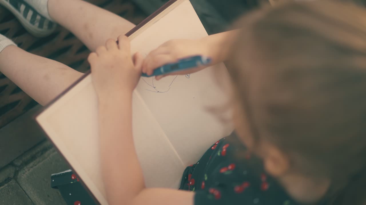 una niña dibuja un sol gracioso en un cuaderno sentada en el pavimento