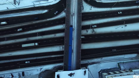 top view of subway train driving on bridge over snowy highway in winter city. metro railways overhead city highway road. winter car traffic from drone above