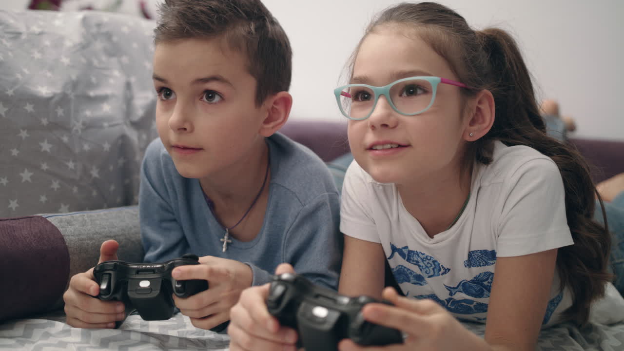 Dzieci grające w gry wideo. Dzieci leżące na sofie z kontrolerami w rękach.