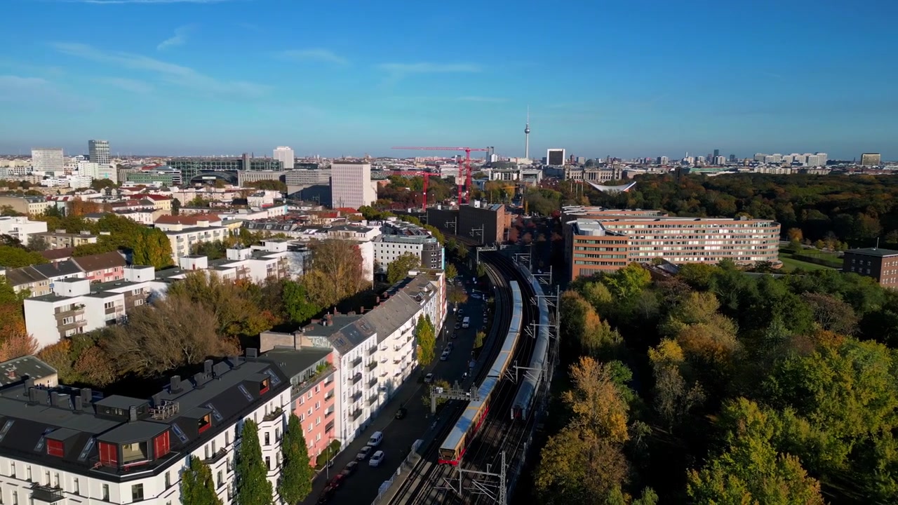 Vista panoramica di un treno che attraversa un ponte su un fiume a Berlino, circondato da un vivace fogliame autunnale. Bella ripresa aerea con rotazione a destra del drone.