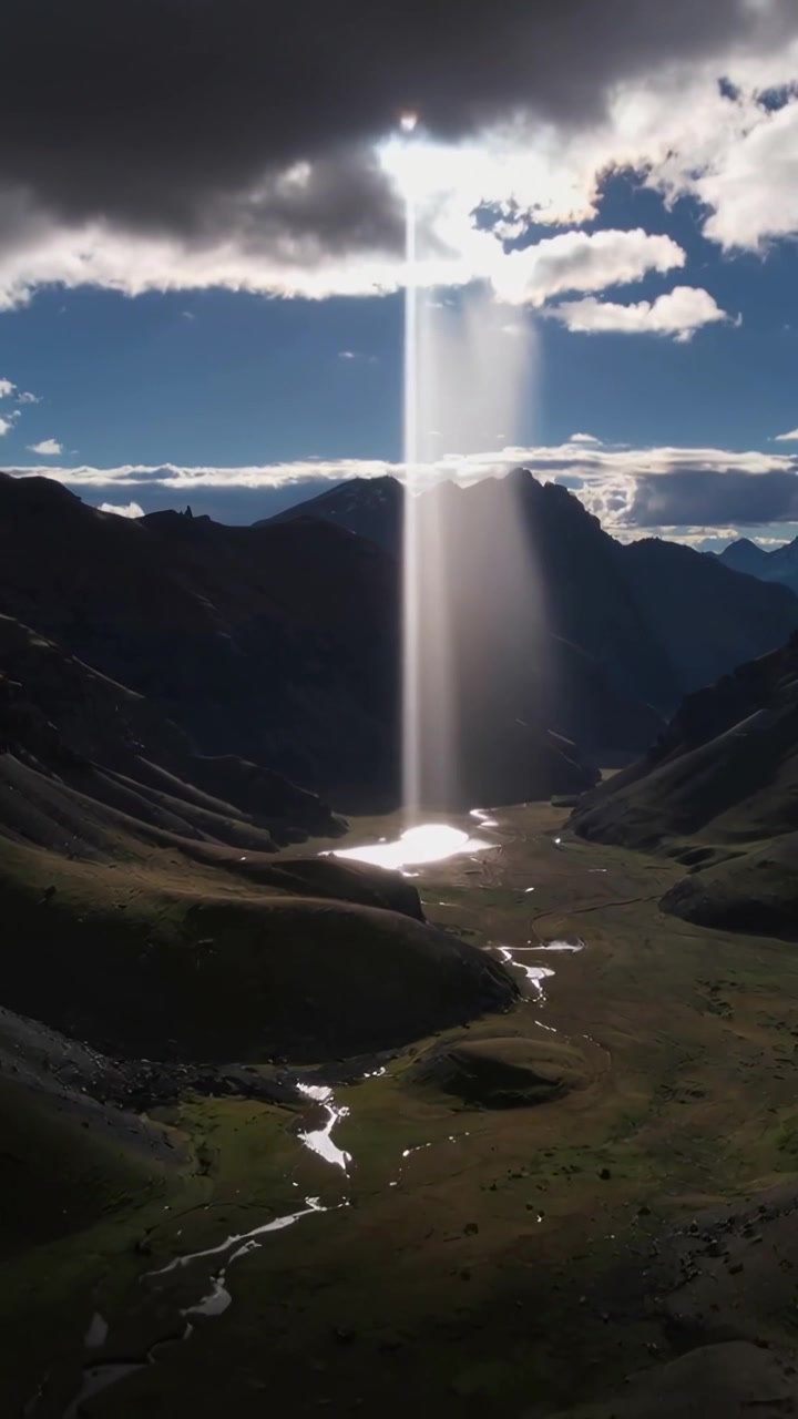 Video verticale: Raggio di sole che si proietta da una fessura tra le nuvole, colpendo un lago in una valle alpina e illuminando un ruscello