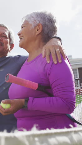 video of happy biracial senior couple embracing and walking with rackets on tennis court