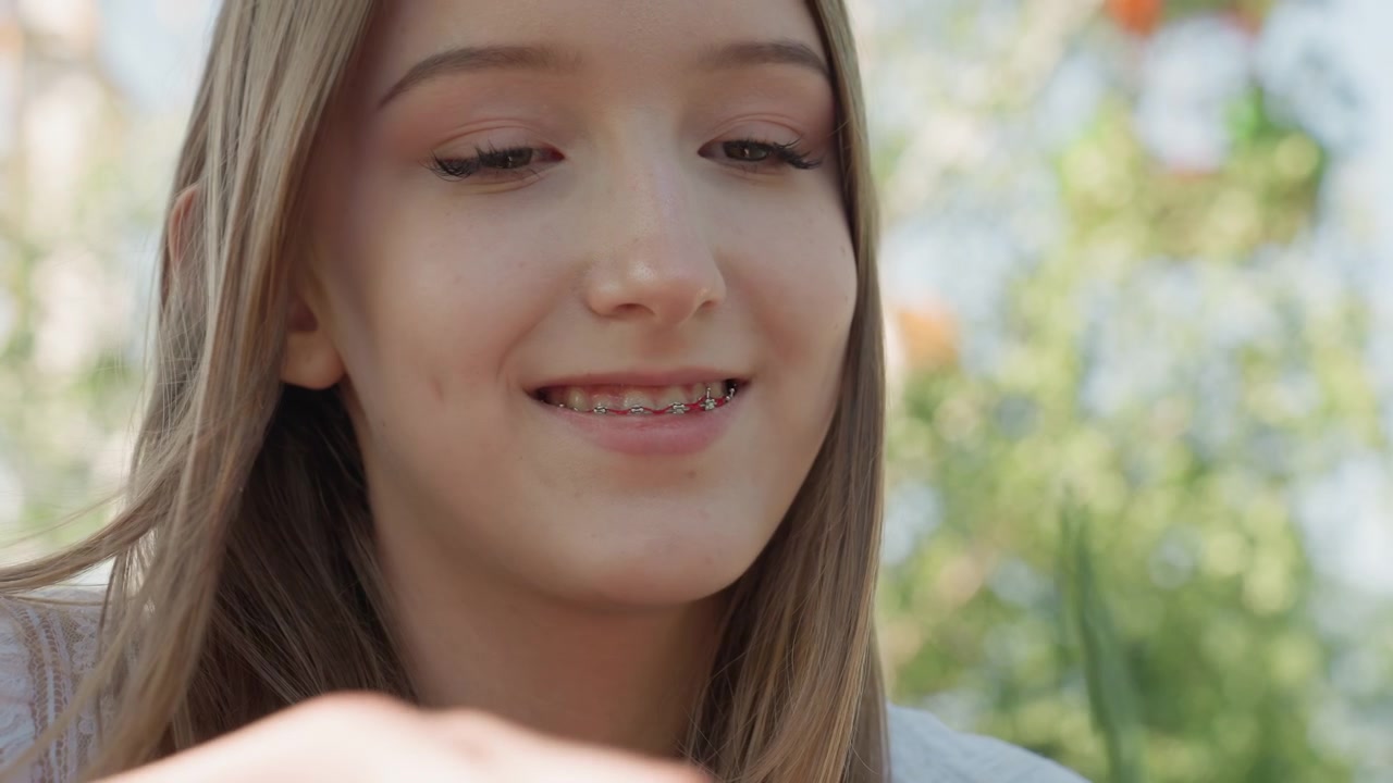 Primo piano di una giovane donna che tiene filati colorati e ferri da maglia, mentre lavora attivamente al suo progetto. Le sue mani si muovono con destrezza con i materiali in un ambiente esterno circondato dalla vegetazione.