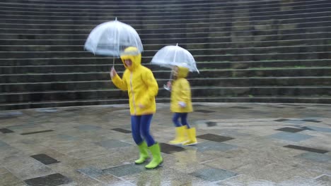 Carefree-kids-in-raincoats-and-umbrellas-having-fun-on-rainy-day