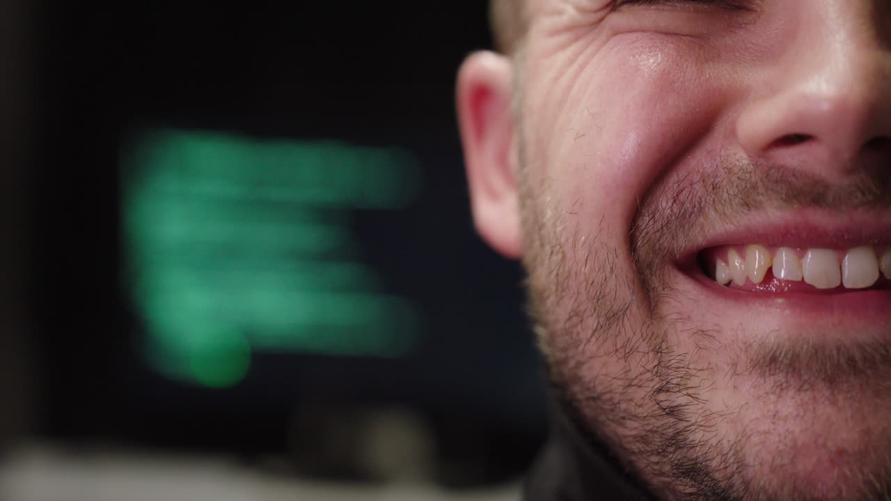 Cinematic close-up of a smiling man with a blurred computer display behind him, suggesting relief and productivity after AI assistance—concept for automation, digital support, and tech optimism