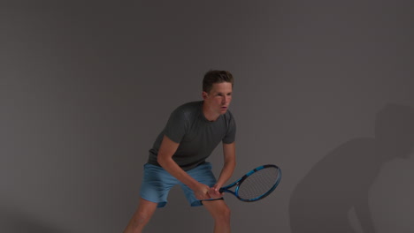 fotografía de estudio de un jugador de tenis masculino devolviendo el tiro en un partido golpeando la pelota con una raqueta contra un fondo gris 2
