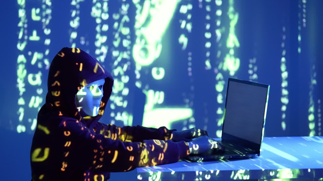 A masked figure in a hooded jacket types on a laptop surrounded by glowing green symbols cascading across a deep blue background, portraying a cyberpunk, futuristic hacking scenario