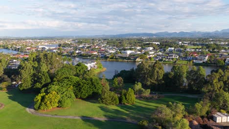 drone footage captures lush greenery, suburban homes, and a serene river under soft daylight in gold coast, australia
