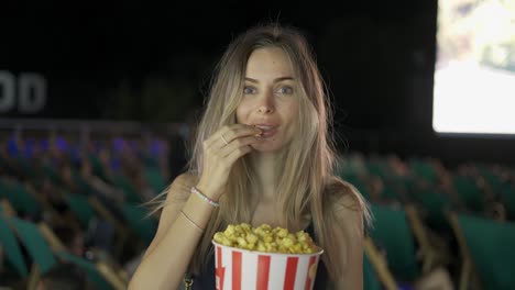 retrato de una encantadora rubia tomando palomitas de maíz dentro de la sala de cine