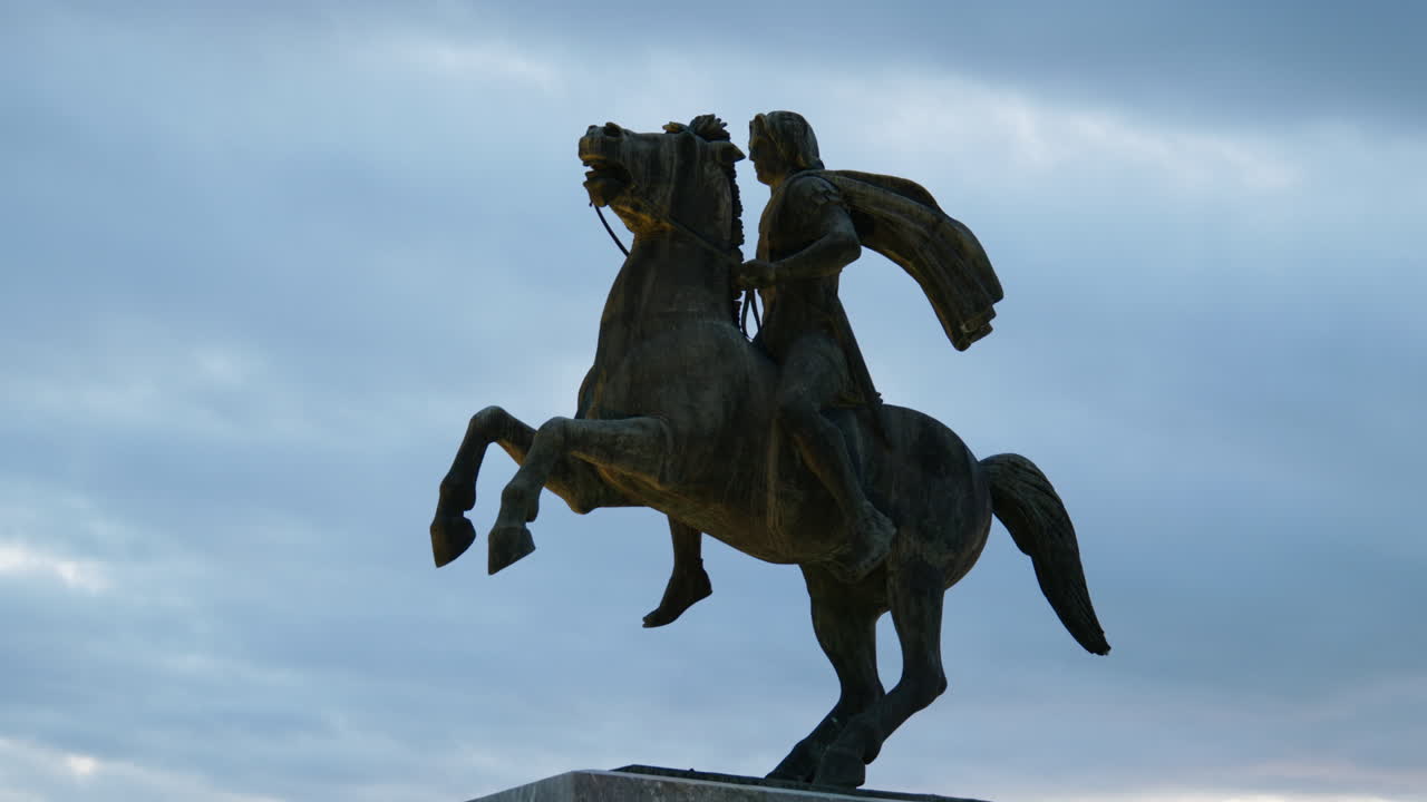 Rearing horse statue of Alexander the Great seen at golden sunset in Thessaloniki with seaside background and visitors.