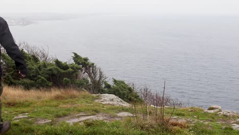 person walks away from the camera and stand on the cliff to think with the ocean as background