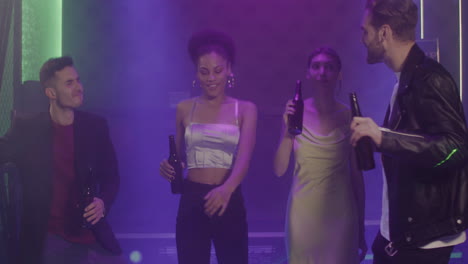 group of four young friends holding beer and dancing at disco