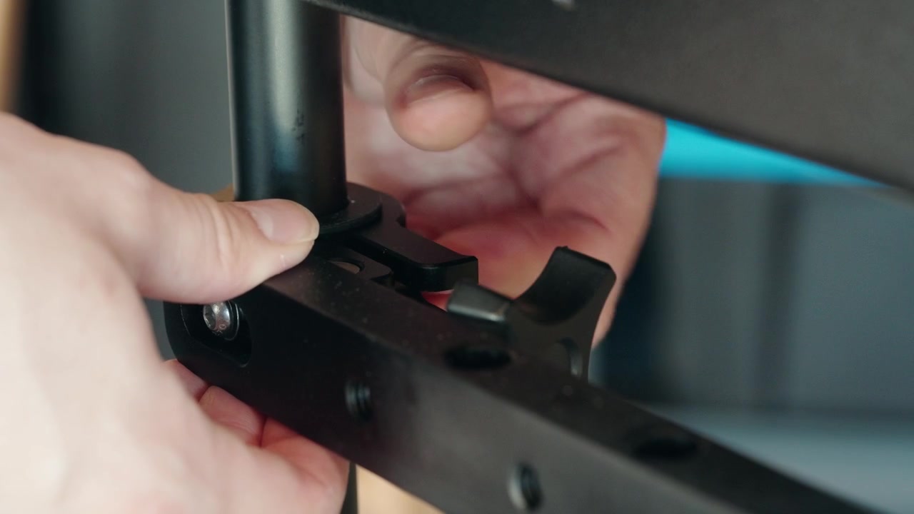 Close-up shot of a man's hands tightening a black plastic adjustment knob to secure a metal bar on industrial equipment