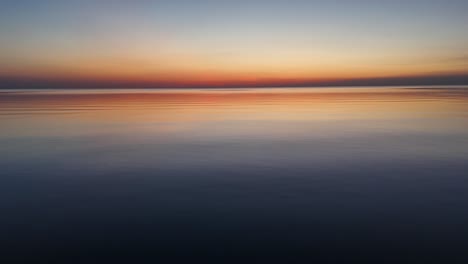 drone shot skimming the surface of a calm lake at sunset